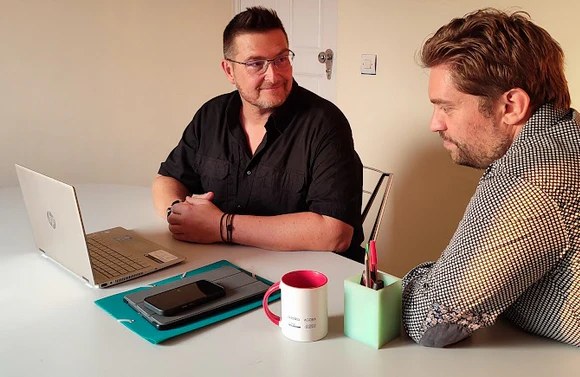 Deux collaborateurs assis à un bureau avec ordinateur portable et téléphone discutant